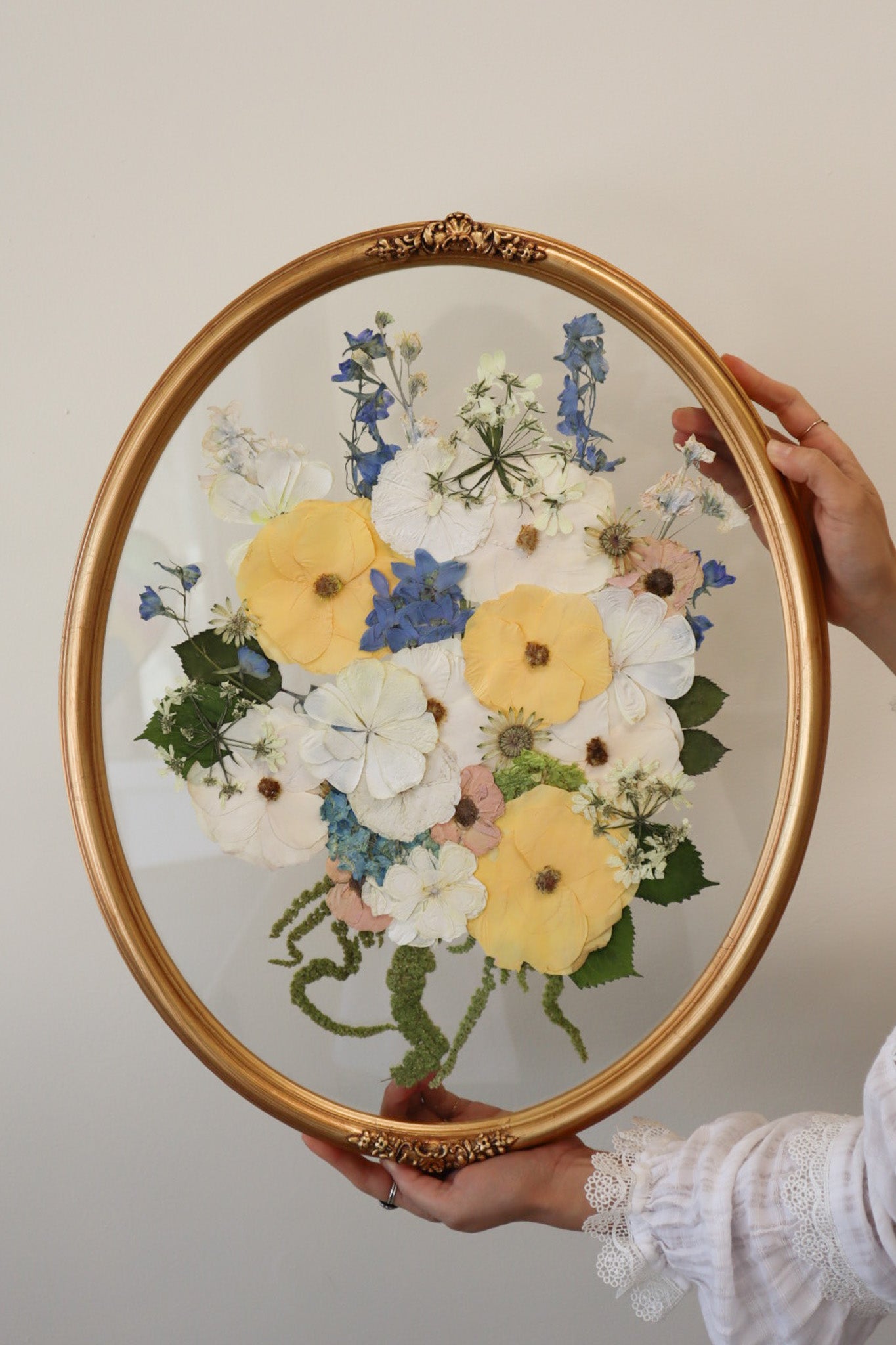 Gold oval frame with pressed flowers against a plain background