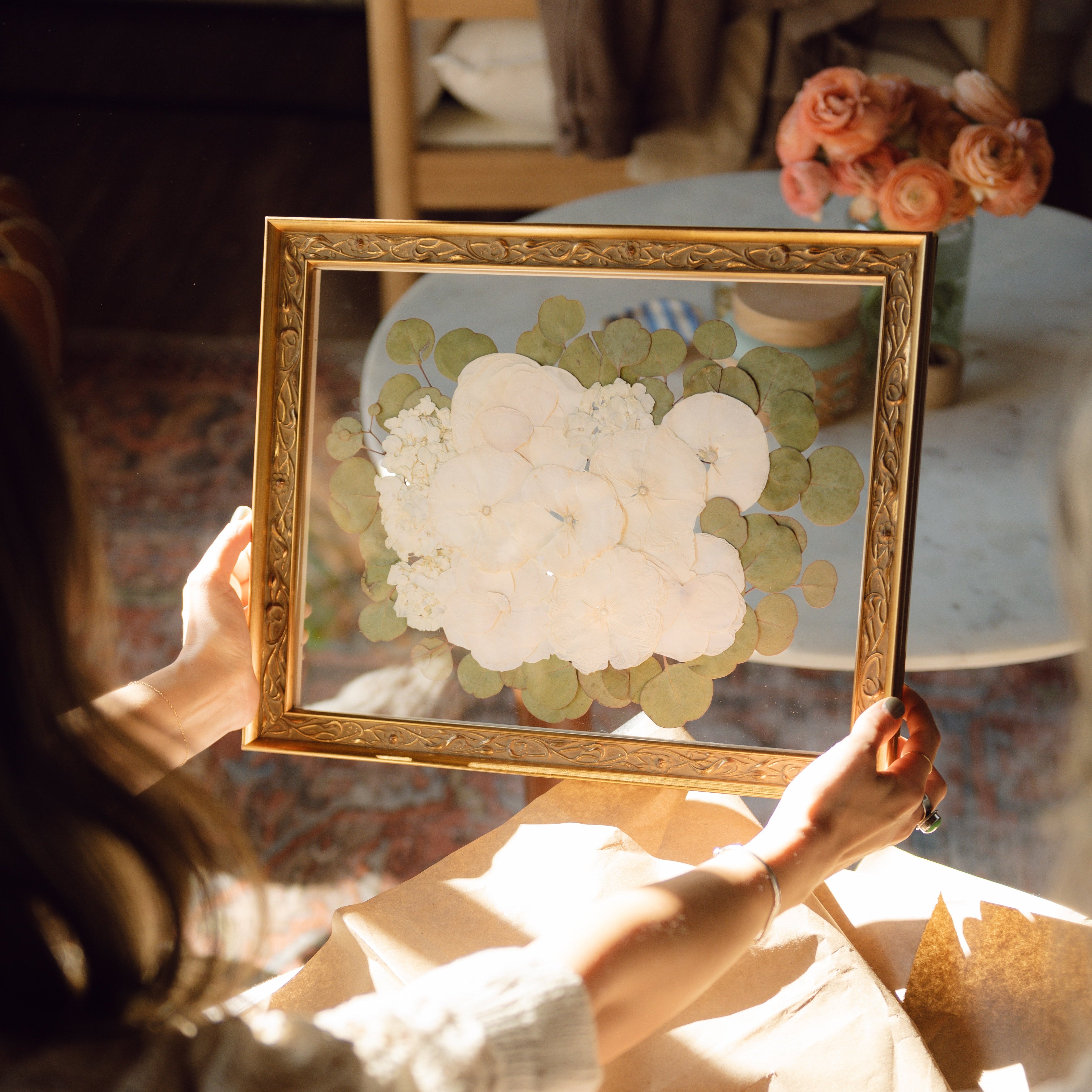 Person holding a framed artwork of white flowers in a warm indoor setting